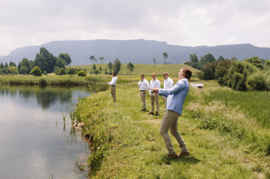 A groom in a light blue suit jacket and beige suit pants fishing with his groomsmen on a lake in Minnesota
